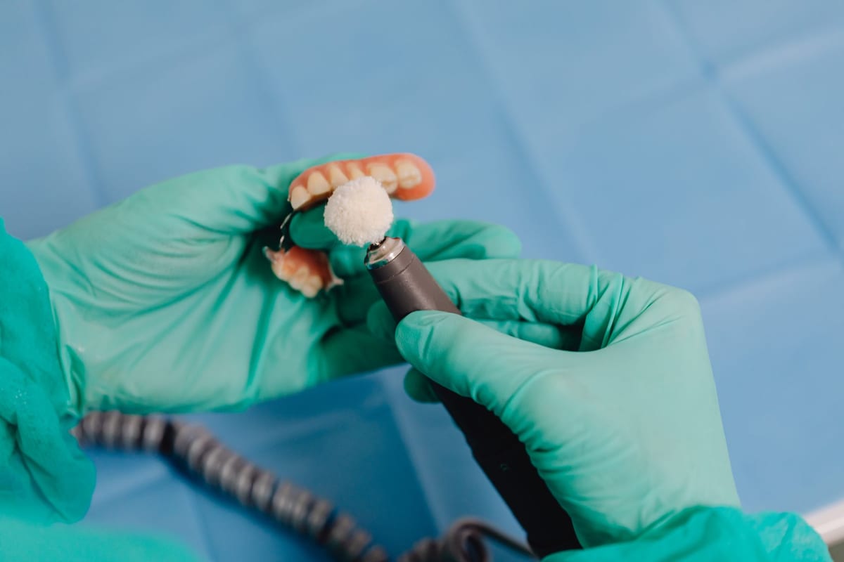 A gloved technician polishing a finished dental restoration with a precision tool
